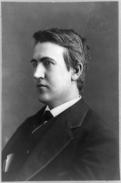 Black-and-white photograph of a young man in profile facing left, with thick tousled hair, a dark coat, a white collar and a dark bow tie.