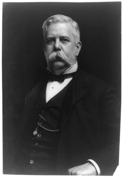 Black-and-white photograph of an older man with white hair and a large white walrus mustache, wearing a dark three-piece suit and a bow tie.